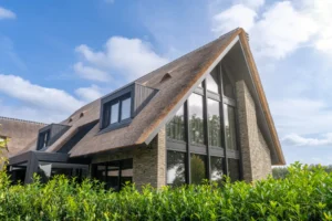 Rietgedekte villa met grote ramen en grijze gevelstenen.