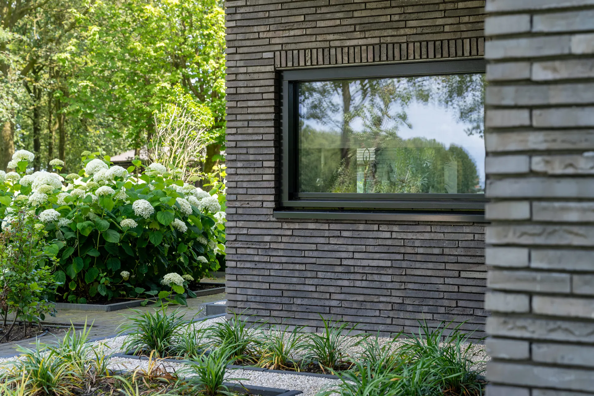 Raam met zwarte omlijsting in een moderne woning, omgeven door donkere langformaat gevelstenen.